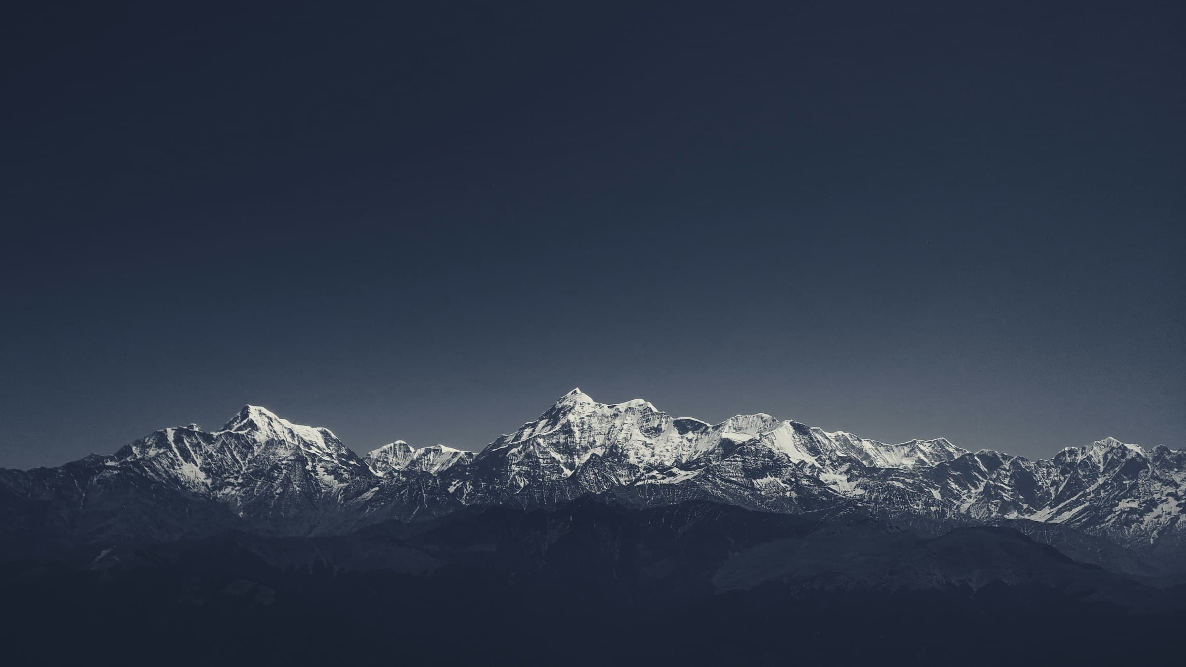 Line of snow-covered Himalayan peaks under a dark blue evening sky