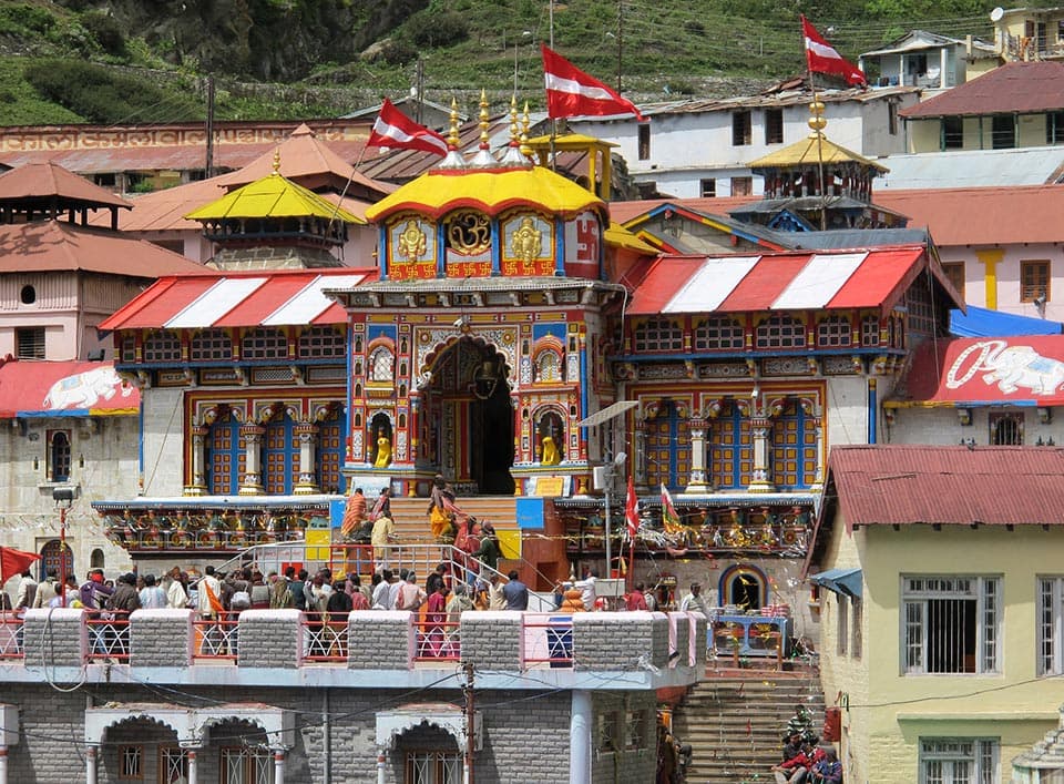 Brightly painted Badrinath temple front with red flags and pilgrims on the steps