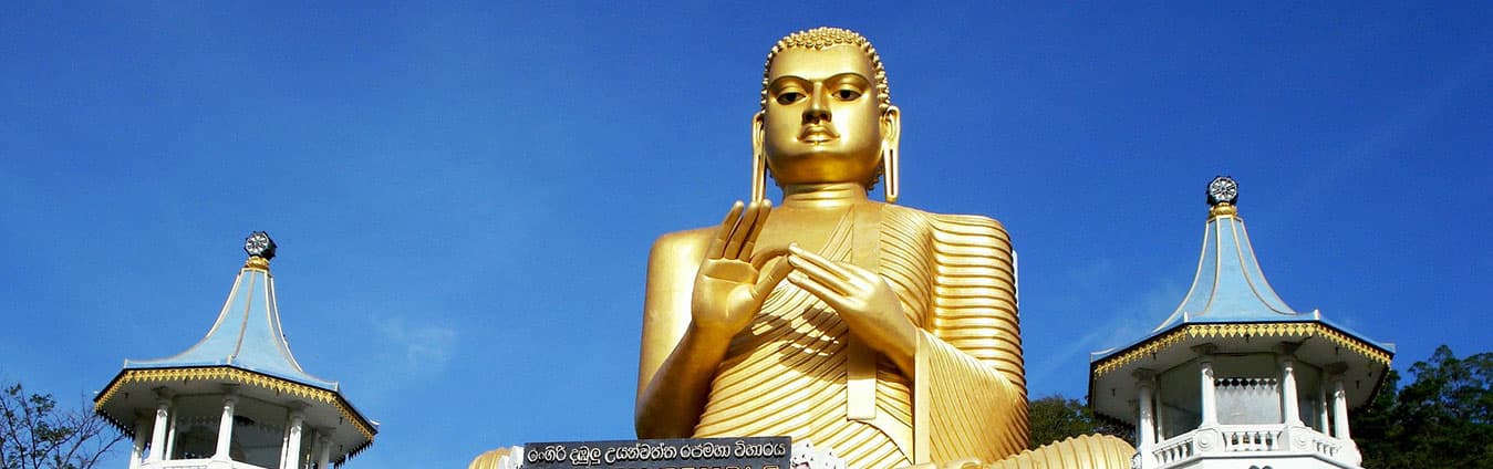 Large golden seated Buddha statue against a blue sky, flanked by two white pagoda towers