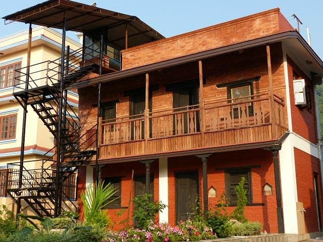 Brick homestay house with a wooden balcony, external staircase and garden flowers in Kathmandu
