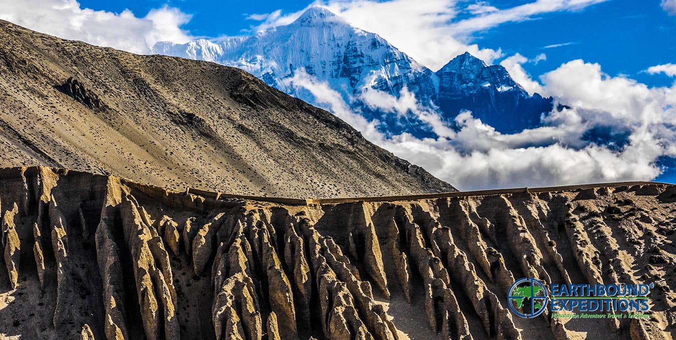 Eroded cliffs and rock pinnacles below snow peaks and clouds on the Jomsom trail