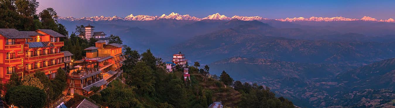 Hillside hotels lit at dusk facing a long line of snowy Himalayan peaks