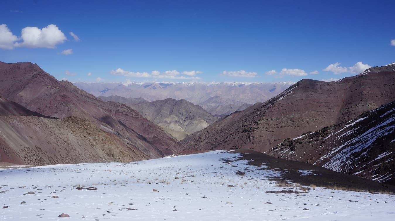Snowy pass looking down a valley of bare brown trans-Himalayan mountains in Ladakh