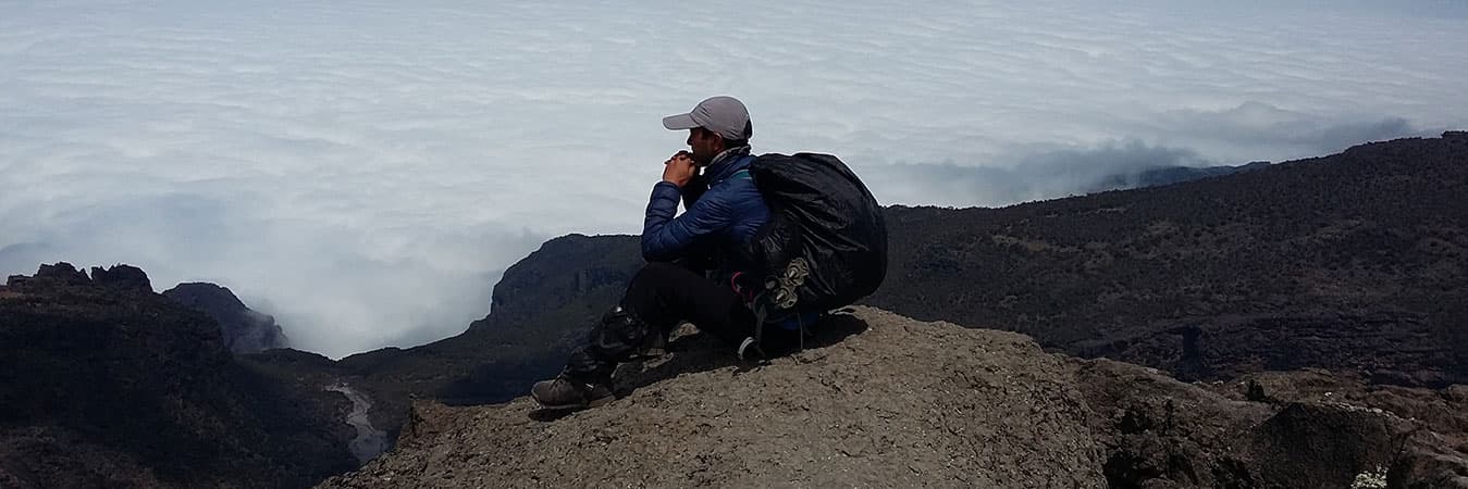 Climber resting on a rocky ridge high above a sea of cloud on Mount Meru