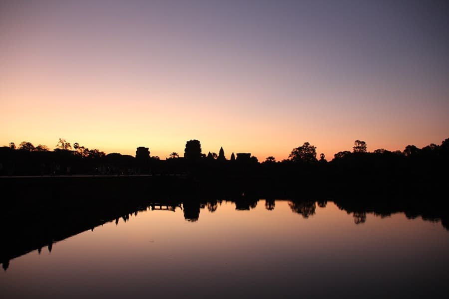 Temple towers and trees silhouetted against a dawn sky and reflected in still water