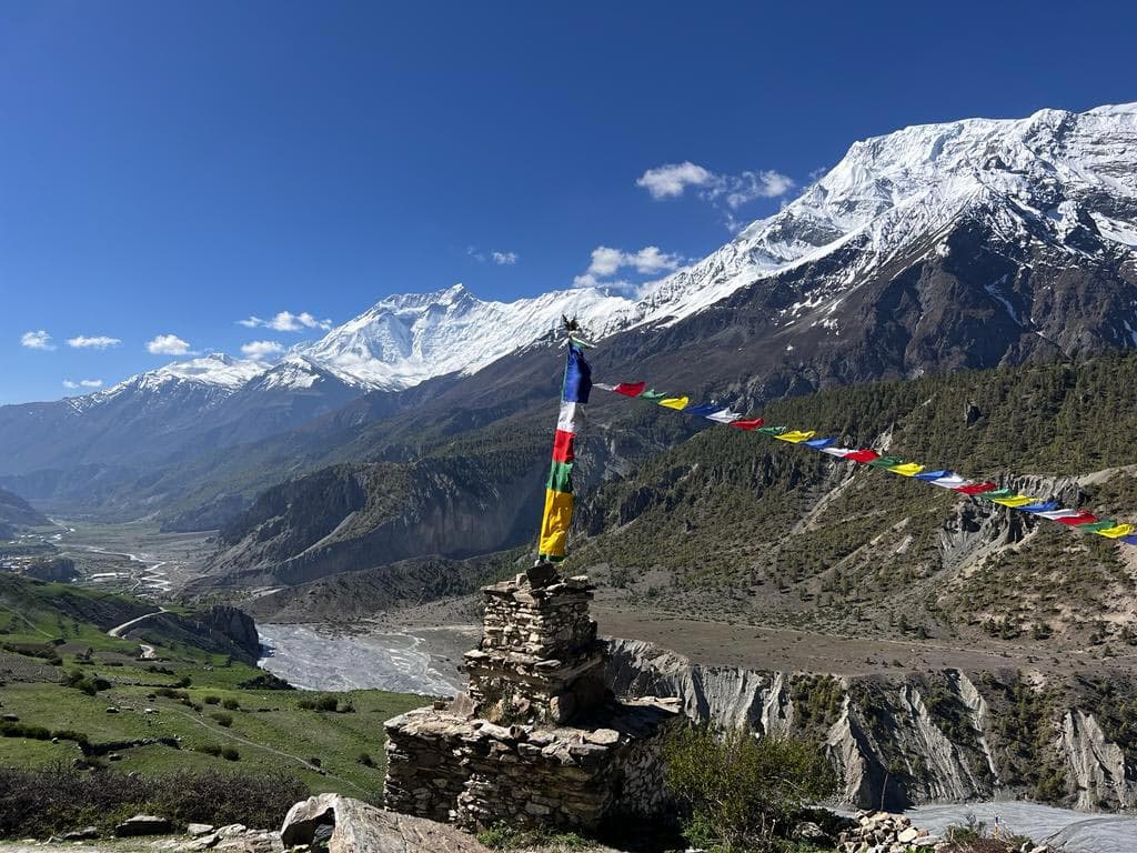 Stone chorten with prayer flags above a river valley and snowy Annapurna peaks