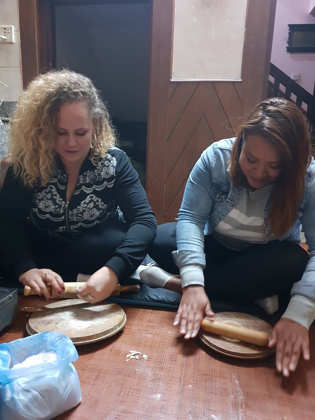 Two women rolling dough on wooden boards during a home cooking class