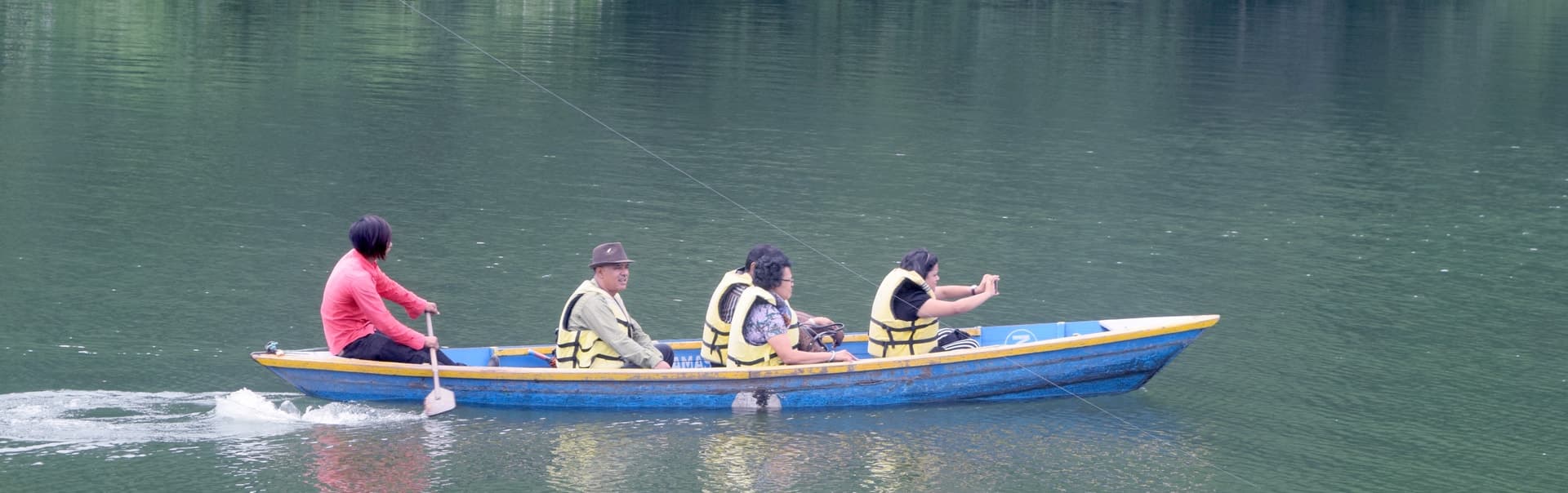 Couple in life jackets in a wooden rowing boat on a calm green lake