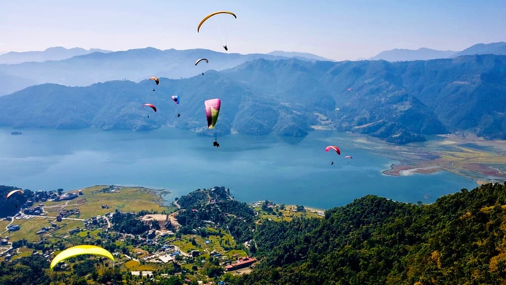 Paragliders over Phewa Lake and green hills near Pokhara on a clear day