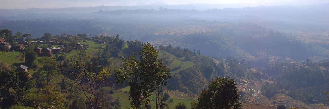 Hazy view over forested hills and scattered village houses from a wooded ridge