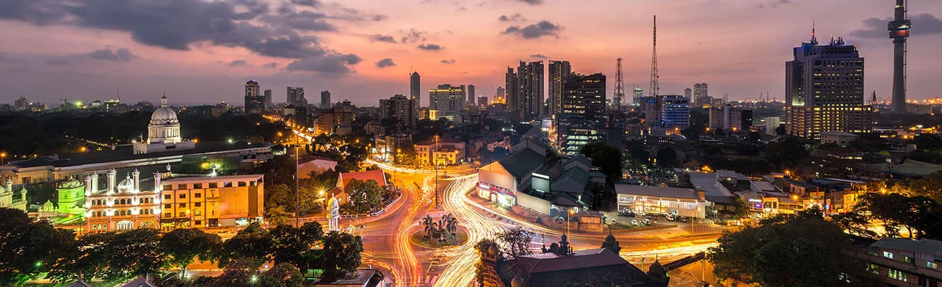 City skyline at dusk with lit roads, towers and a domed building under a pink sky