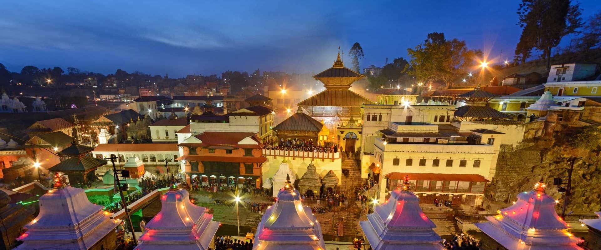 Pashupatinath temple complex lit at dusk with small white shrines in the foreground