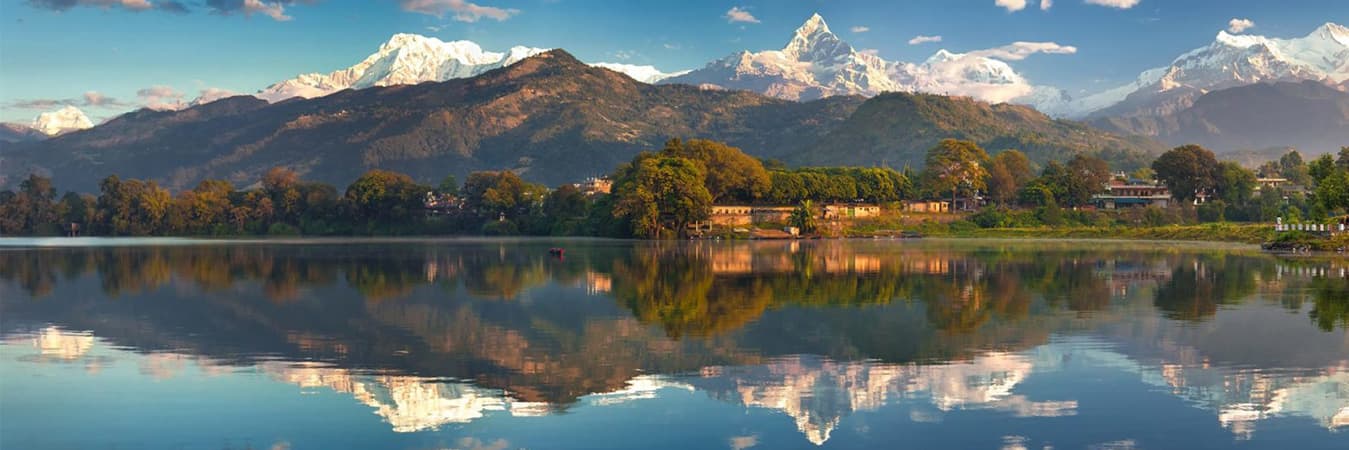 Phewa Lake reflecting Machhapuchhre and the Annapurna range with lakeside trees