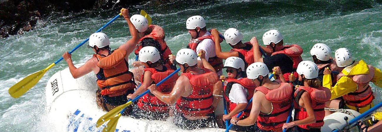Rafters in white helmets and red life jackets paddling hard through rough white water