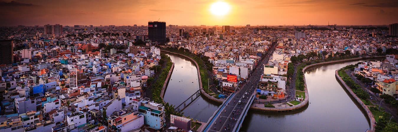 Aerial view of a dense Vietnamese city and its canals under a setting sun