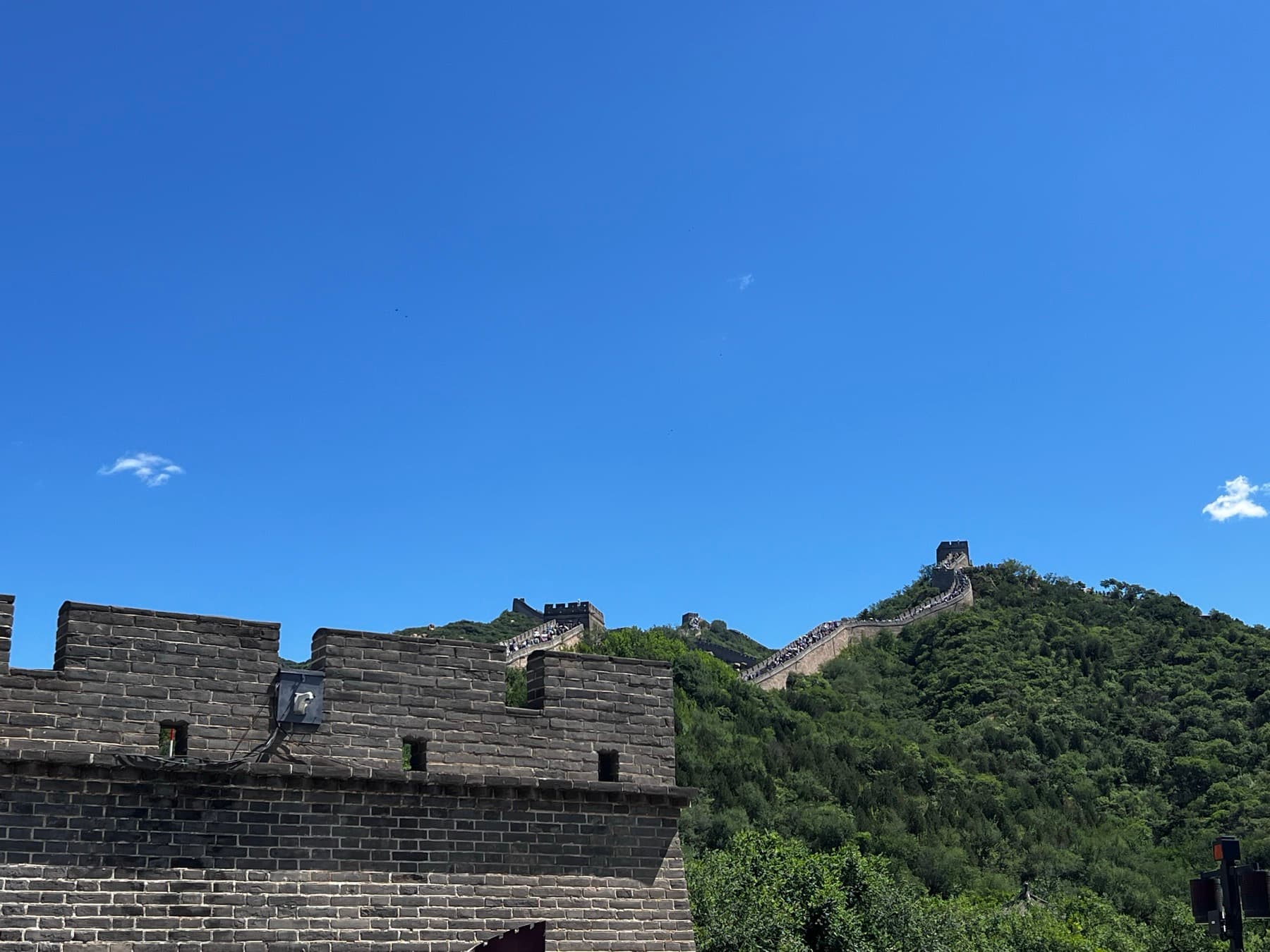 Great Wall of China climbing a green forested ridge beneath a clear blue sky