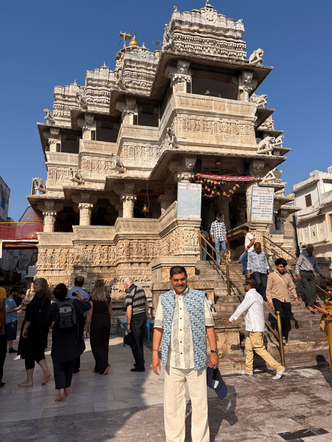 Man standing before a carved white stone Hindu temple with visitors on its steps