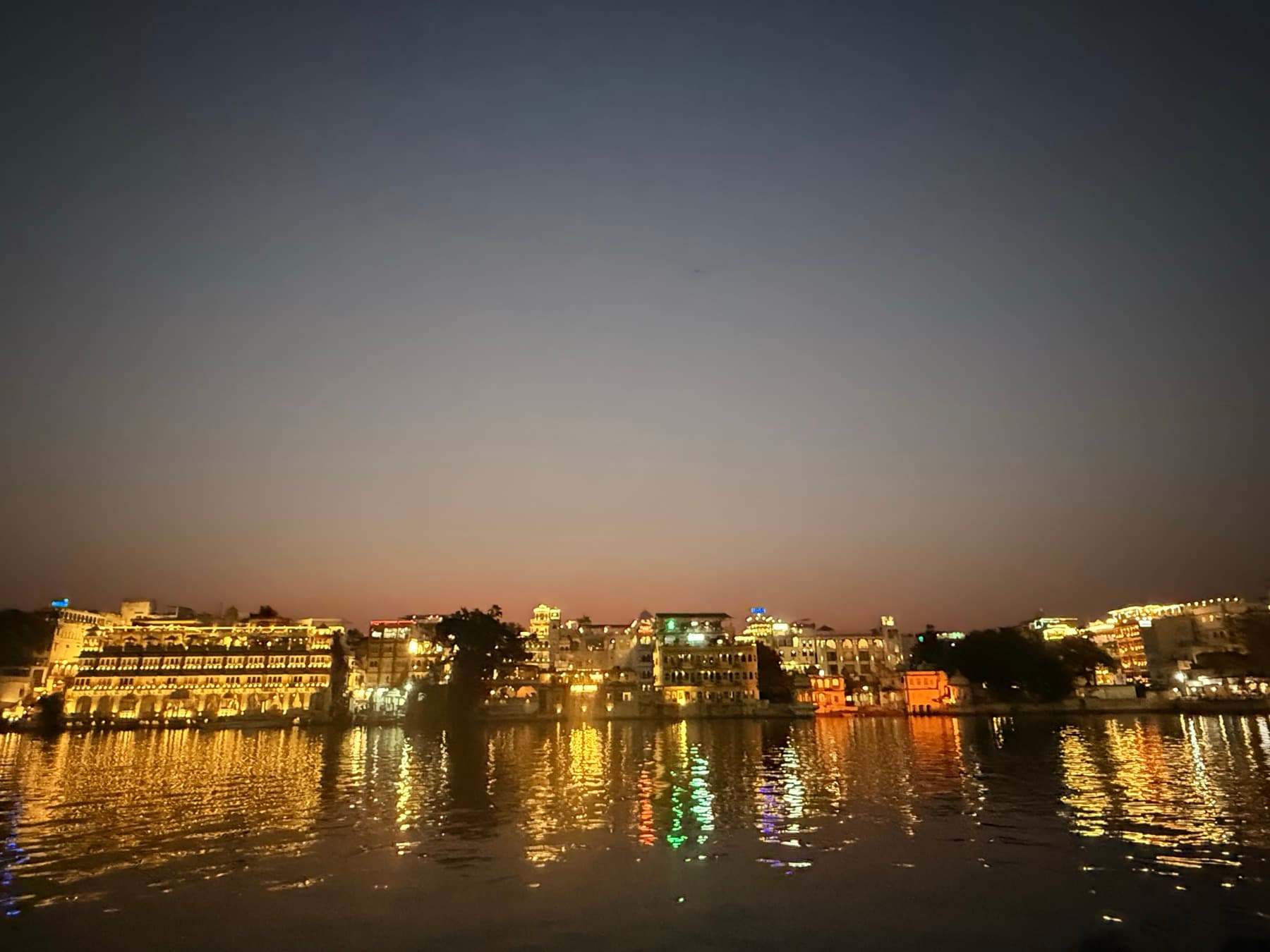 Lakeside palaces in Udaipur lit at dusk and reflected in the calm water