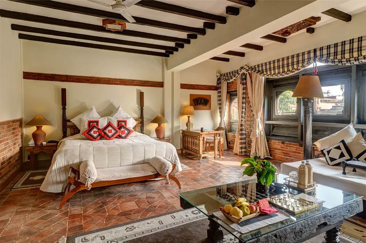 A guest room in a luxury lodge in Nepal, with a carved wooden bed and terracotta floor