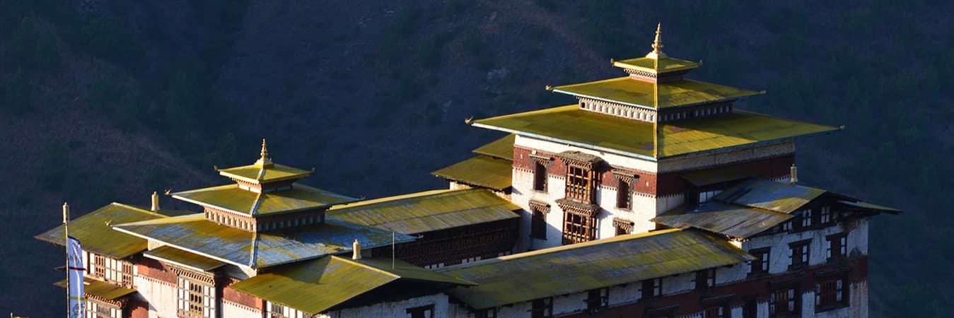 Golden roofs of a whitewashed Bhutanese dzong lit by low sun against a dark hillside