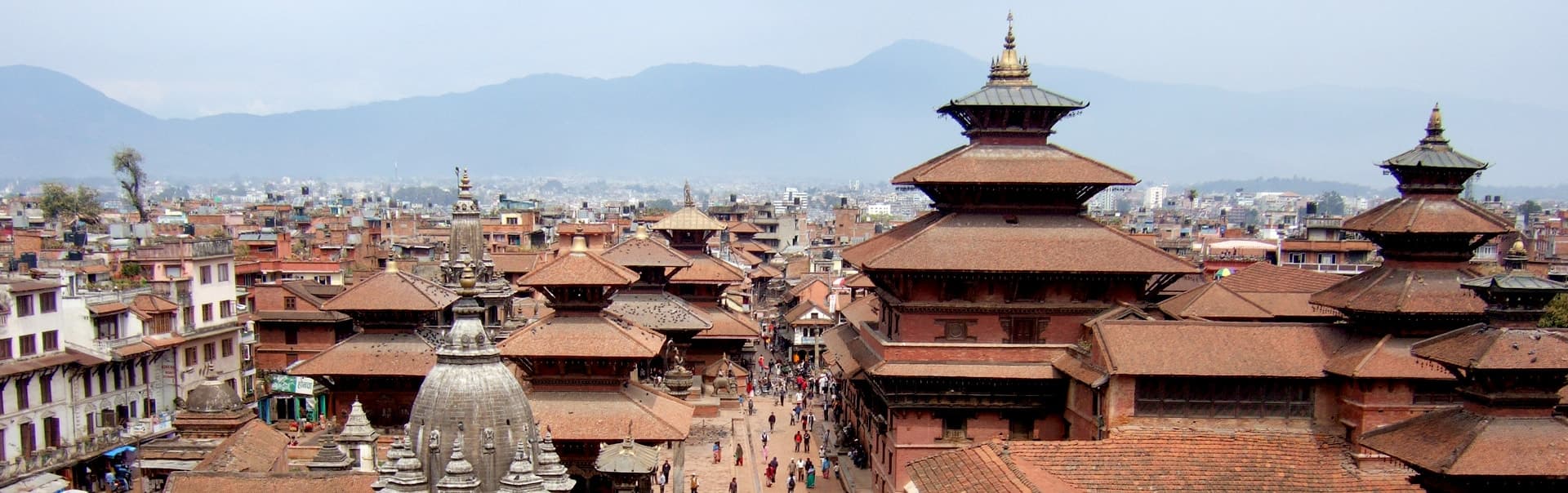 Pagoda temple roofs and brick buildings of Patan Durbar Square with hills behind