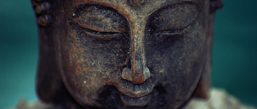 Close view of a weathered stone Buddha face with eyes closed against a teal background