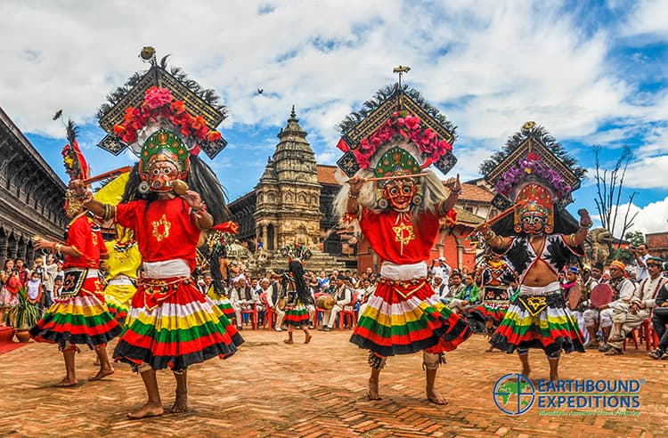 Masked dancers in red costumes and tall floral headdresses performing in a Newar temple square