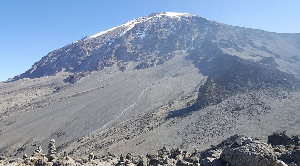Snow-capped summit of Kilimanjaro above a wide grey scree slope and rock cairns