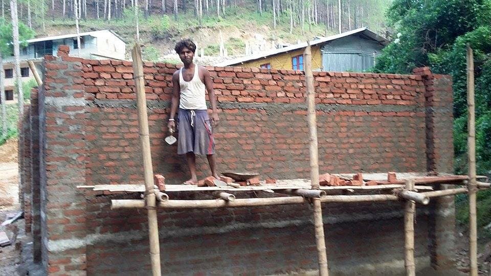 Builder on bamboo scaffolding beside new brick walls of a school building on a hillside