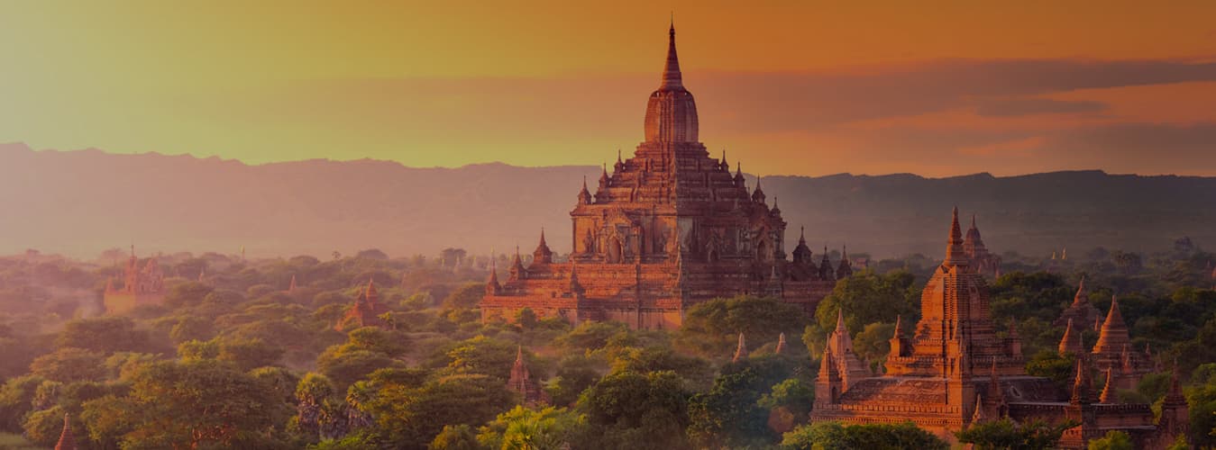 Ancient temples of Bagan rising above the trees in orange evening haze