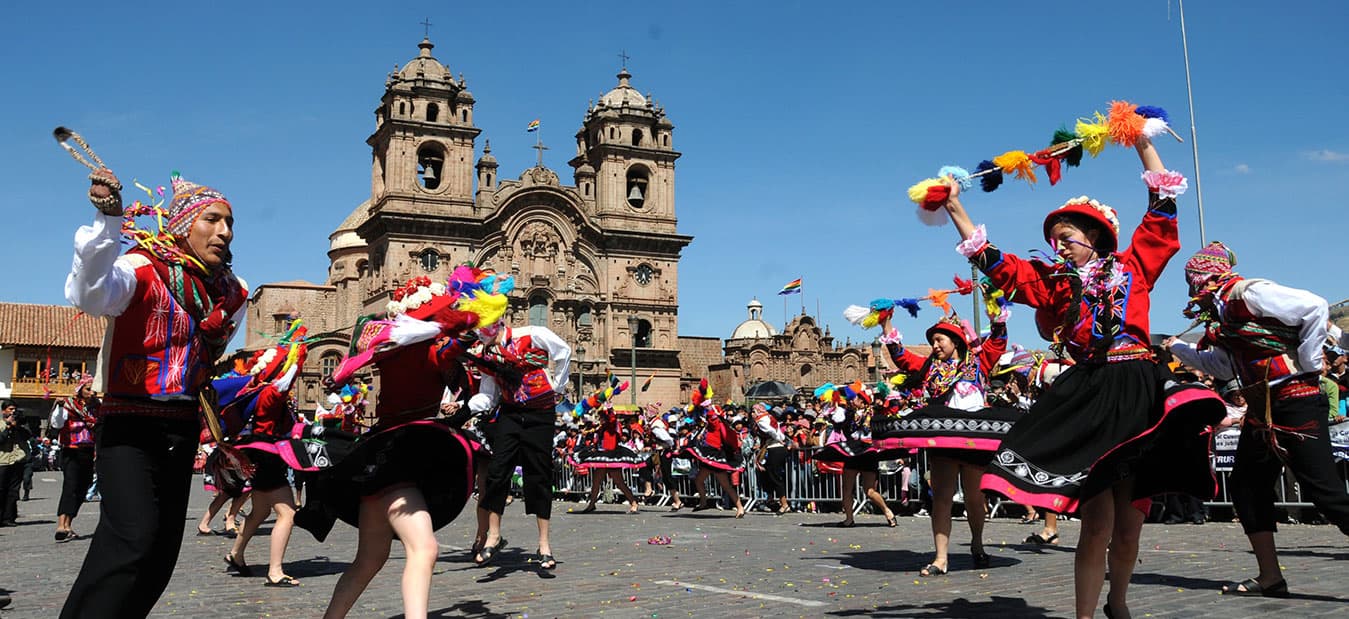 Dancers in bright traditional costume performing in a square before a colonial church in Peru