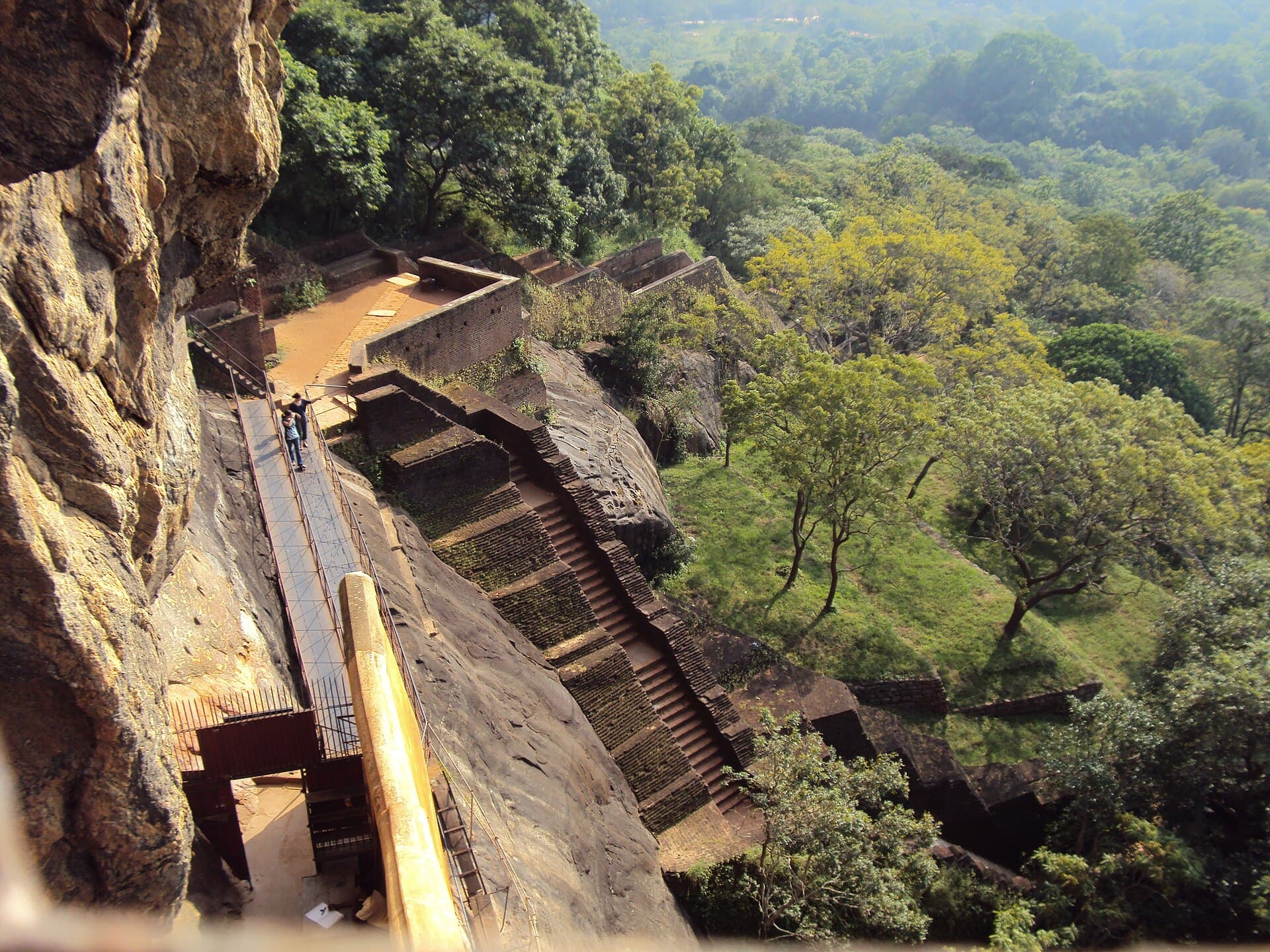 Staircases and walkways on the side of Sigiriya rock overlooking forest and the water gardens