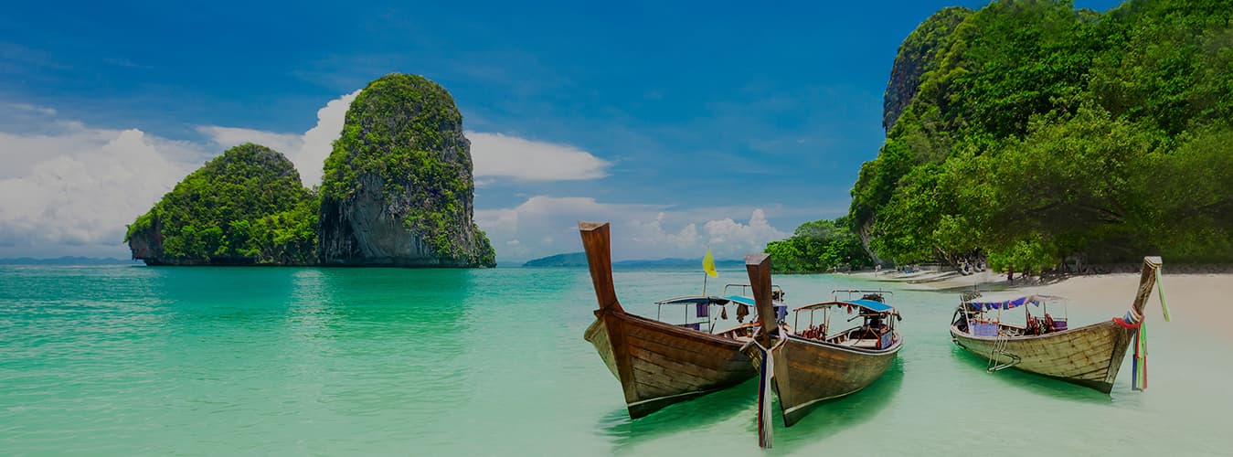 Wooden longtail boats on turquoise water by a sandy beach and limestone islands